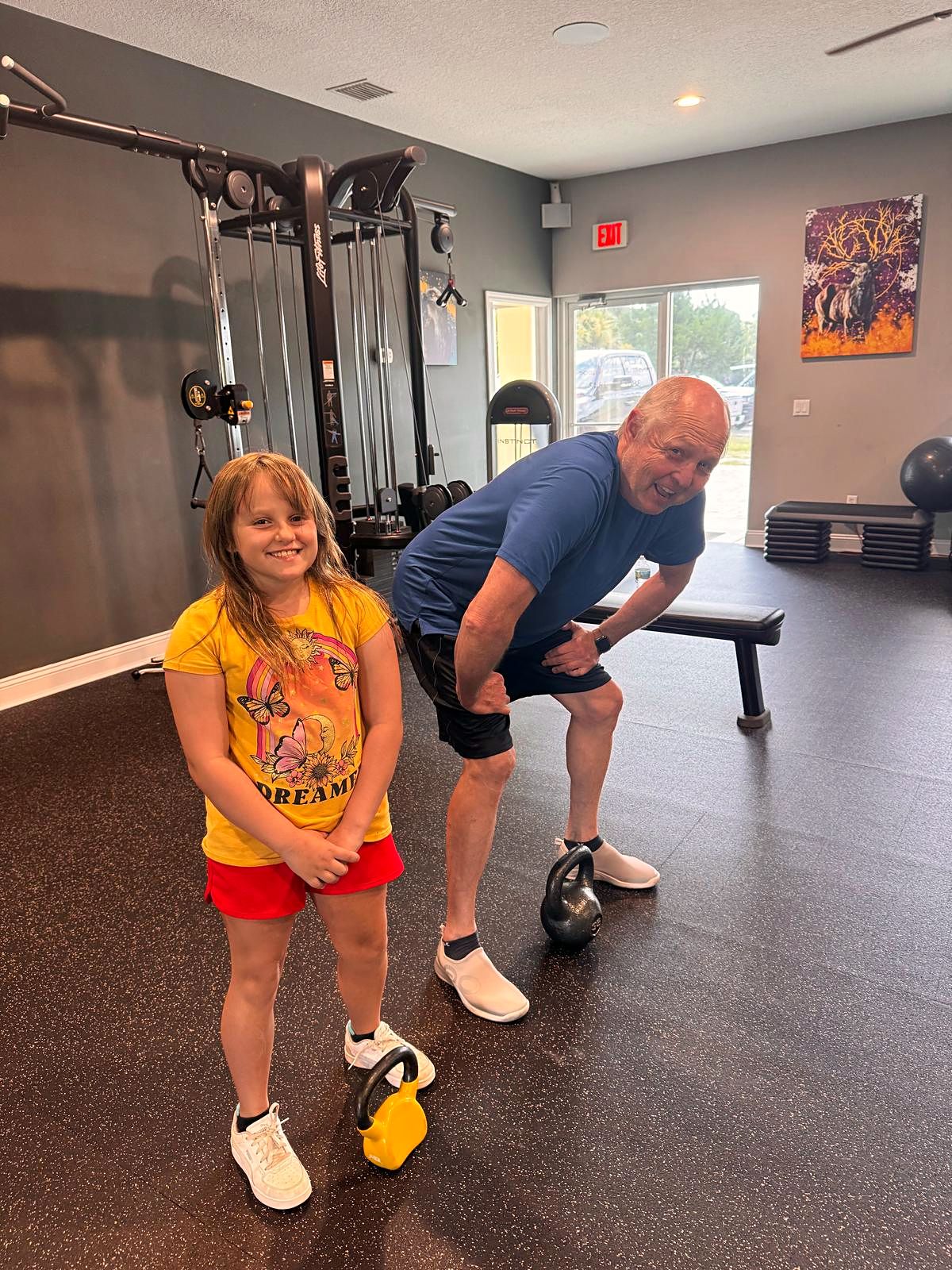 Young girl holding a kettlebell next to a smiling man in the training studio