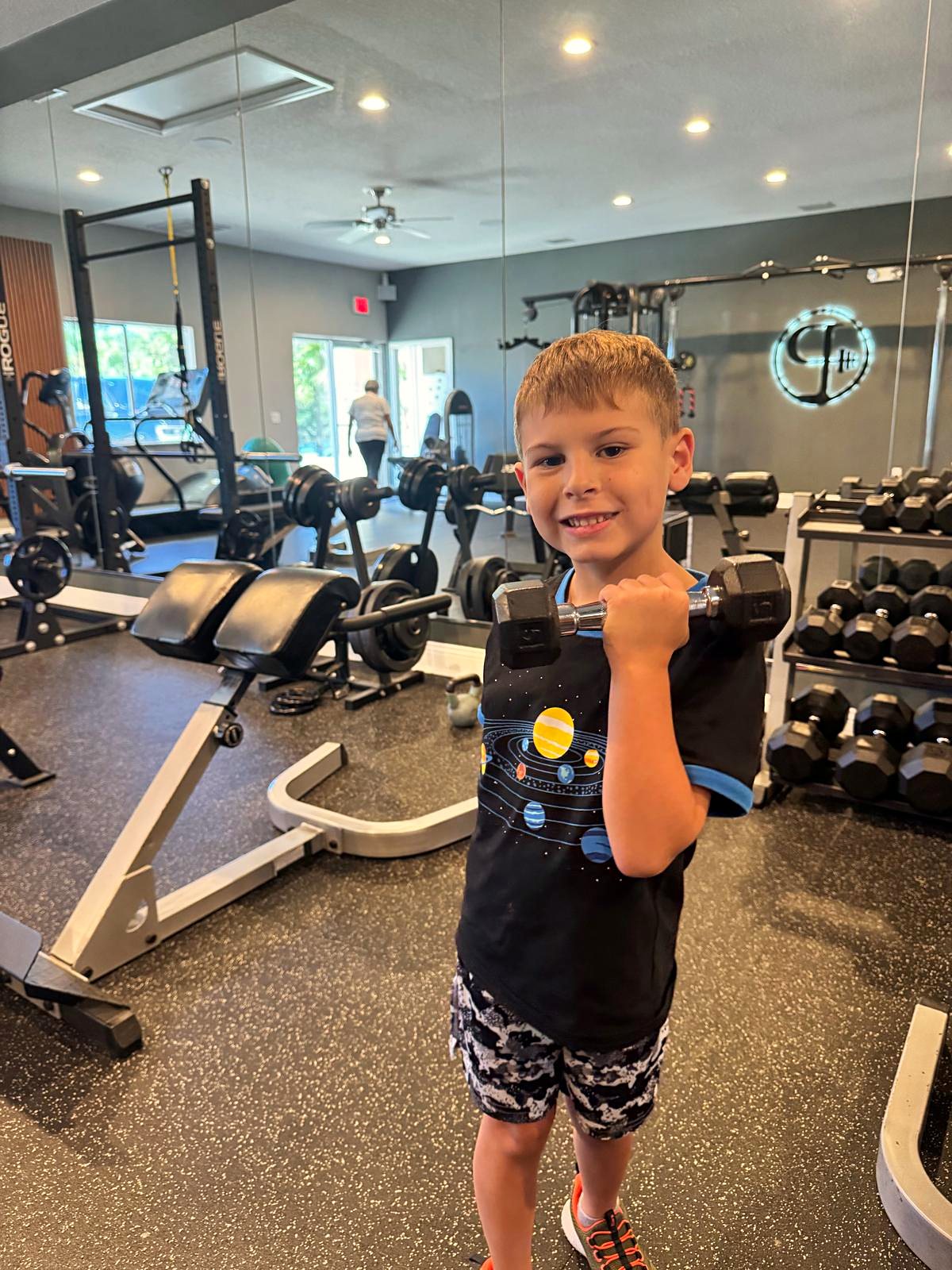 Young boy flexing his arm among the dumbbell racks at Platinum